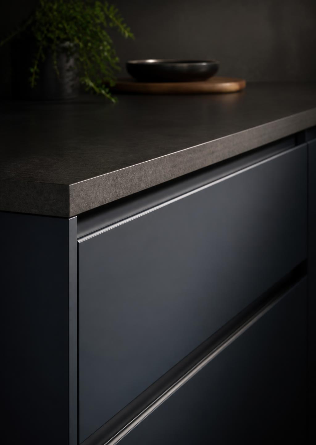 Dark kitchen cabinetry with a laminate worktop edge in low directional light